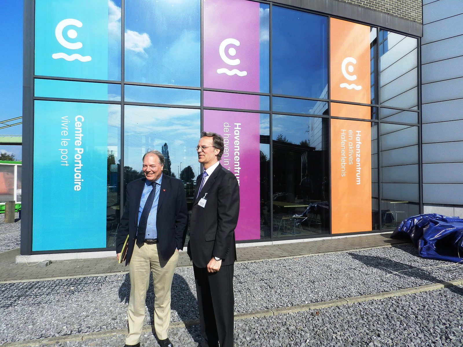 De directeur rechts en de gedeputeerde voor de gevel met het nieuwe logo