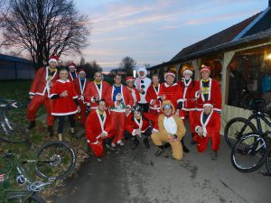 De fgroep verkleed in kerstman (en vrouw) poseert bij de Leeuw van Vlaanderen terwijl de zon ondergaat.  